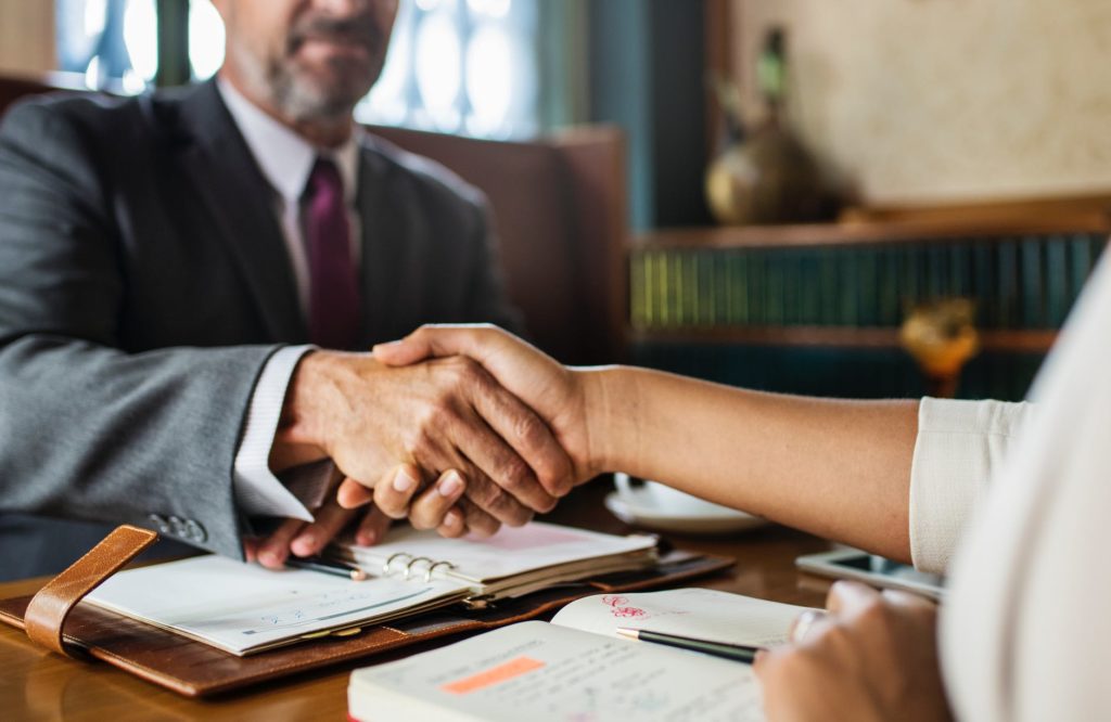 Two professionals in suits shaking hands over a contract on a desk, representing a successful business endorsement deal